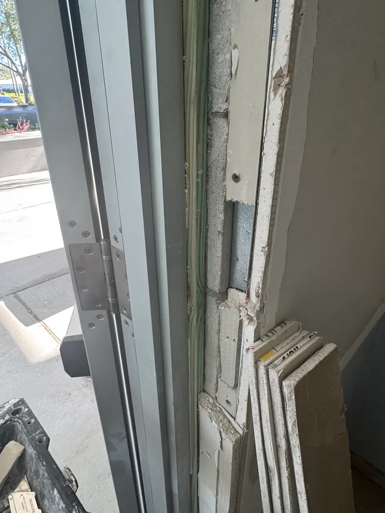 Drywall torn off the jamb of a commercial storefront door, exposing framing, track and old corner bead